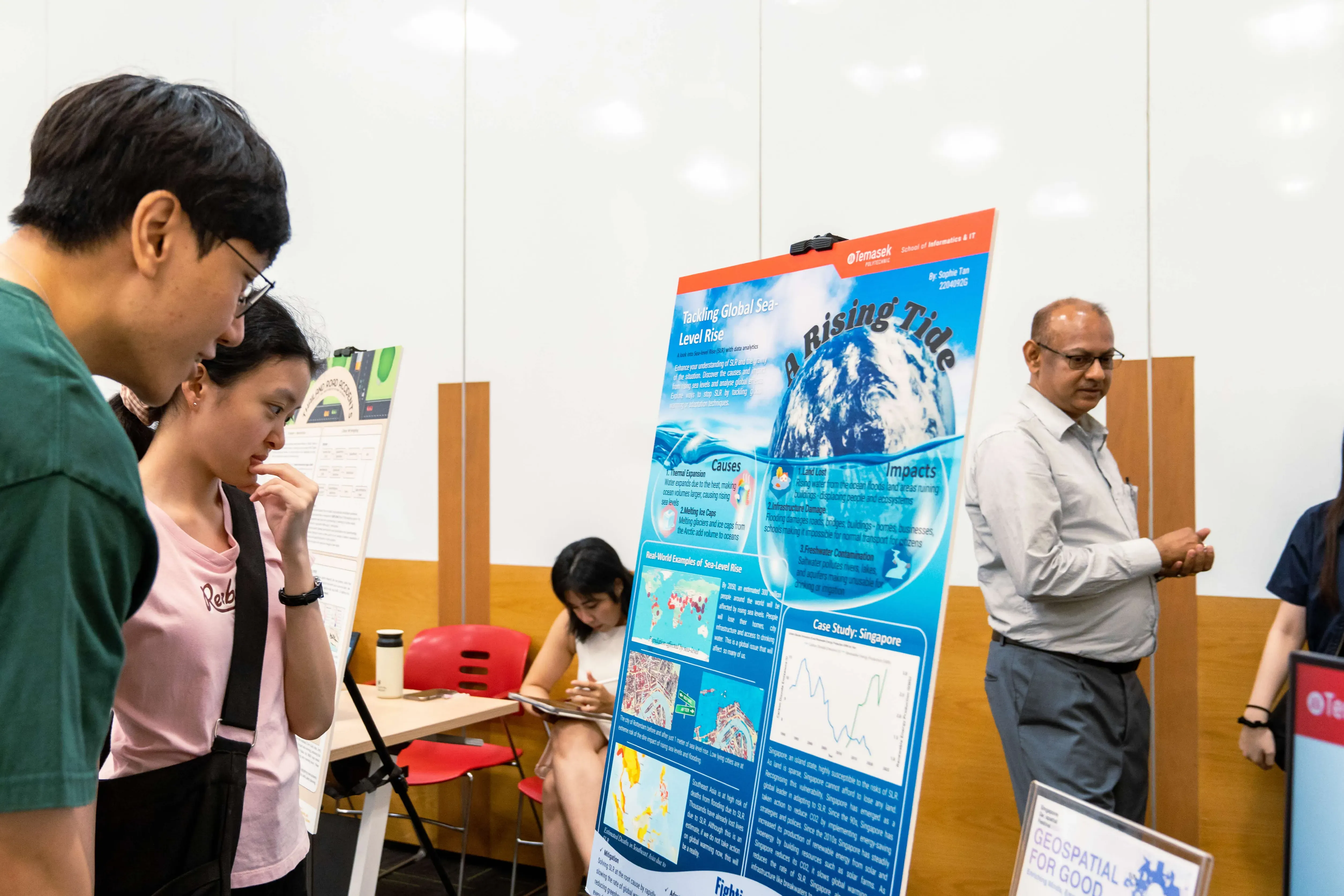 Two students examine a poster titled "A Rising Tide" about tackling global sea-level rise at an academic fair.